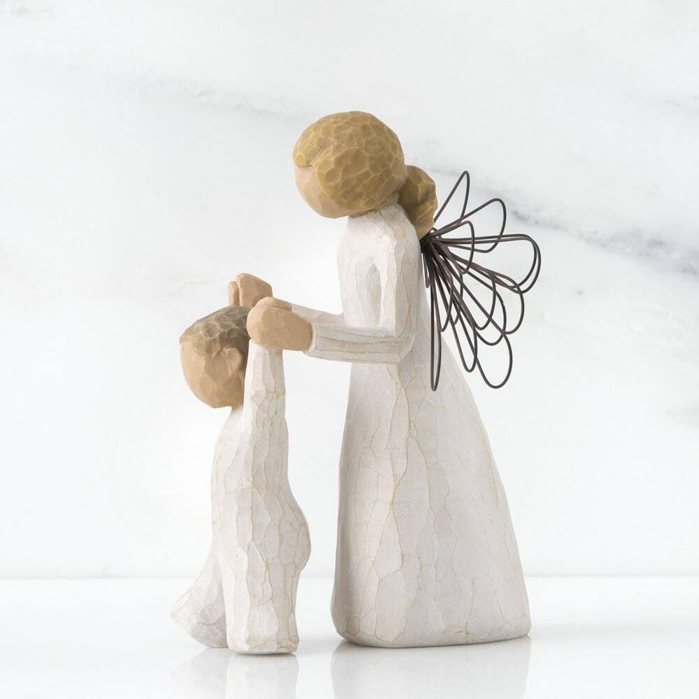 Guardian Angel by Willow Tree. Side View - Female angel in cream dress and wire wings, holding both hands of toddler in cream onesie walking in front of angel