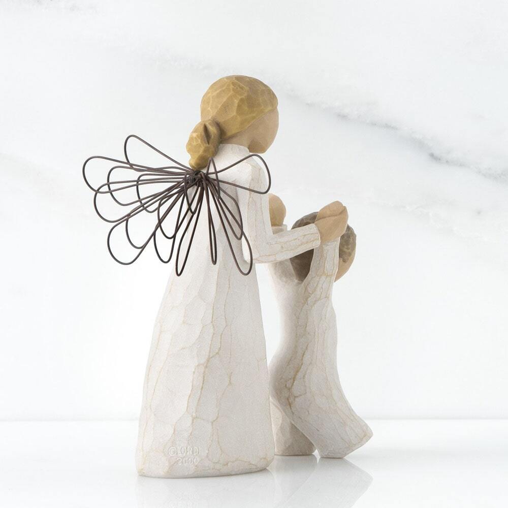 Guardian Angel by Willow Tree. Back View - Female angel in cream dress and wire wings, holding both hands of toddler in cream onesie walking in front of angel