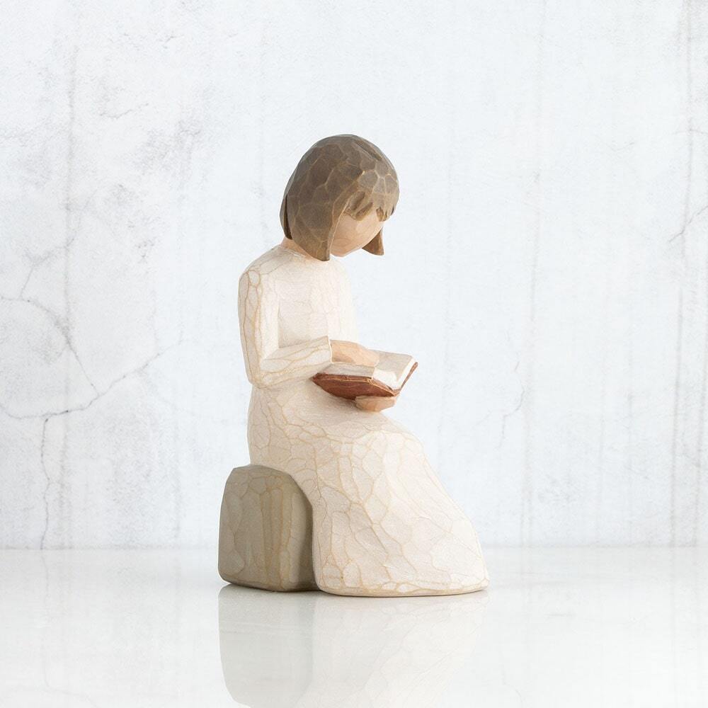 Wisdom by Willow Tree. Figure in cream dress seated on a gray rock, reading a book