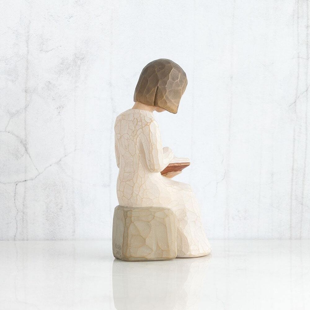 Wisdom by Willow Tree. Figure in cream dress seated on a gray rock, reading a book
