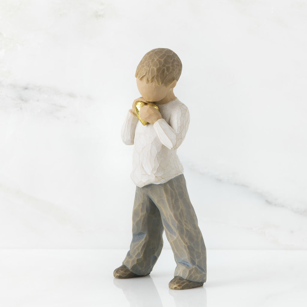 Heart of Gold by Willow Tree. Standing boy figure in cream shirt and blue jeans, holding gold-leaf heart with both hands to his chest