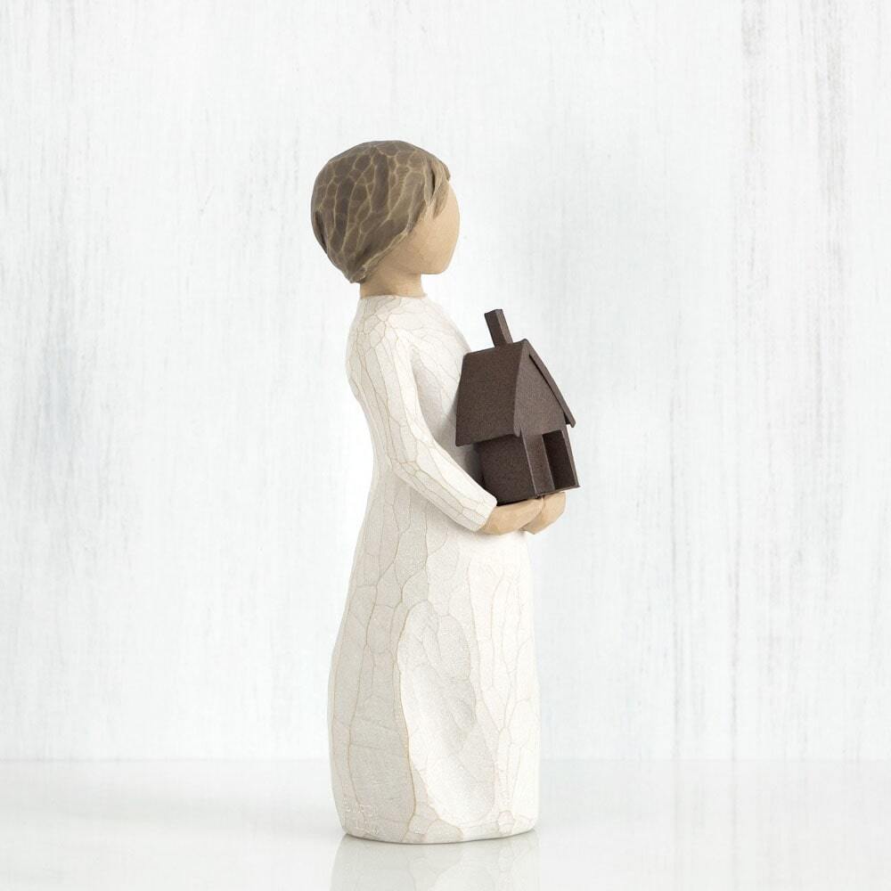 Mi Casa by Willow Tree. Standing figure in cream dress, holding dimensional metal house with chimney and open front door in her arms