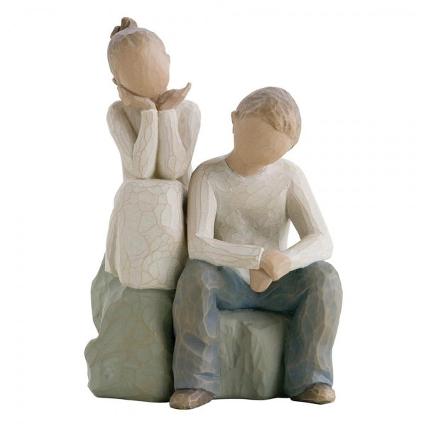 Figure of boy and girl, seated on a gray rock next to each other. Girl in cream dress, boy in cream shirt and blue jeans