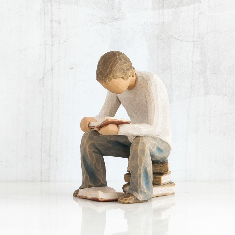 Figure of young man in cream shirt and blue jeans, seated on stack of books, reading book