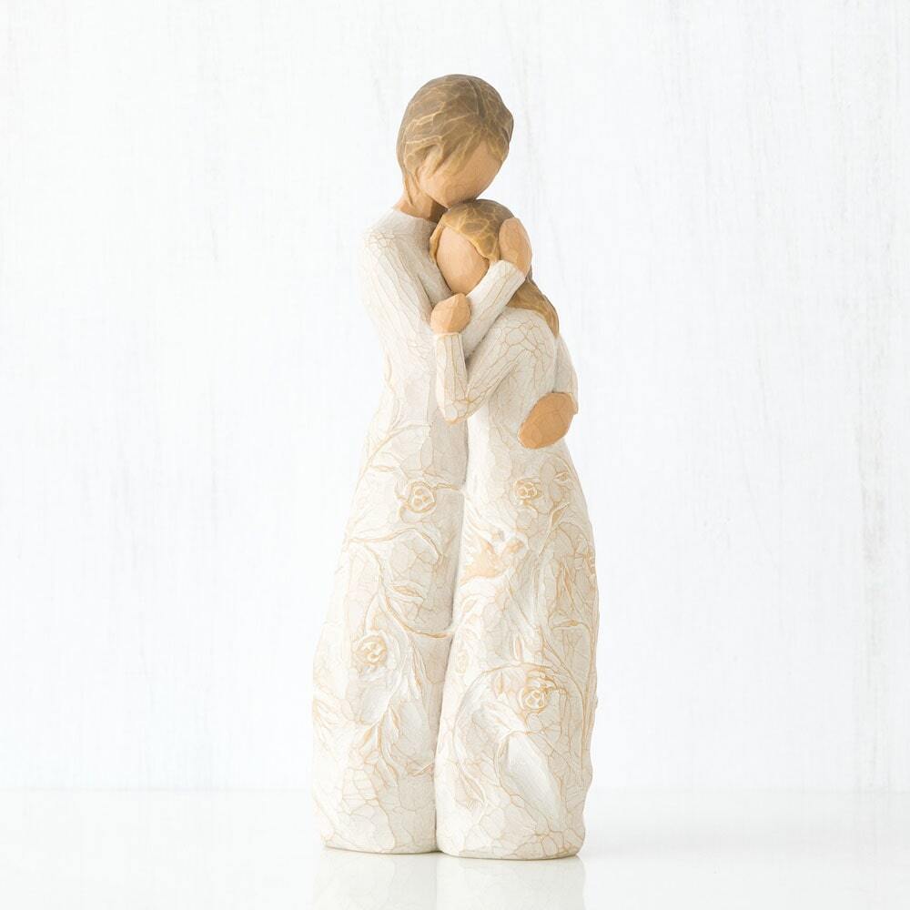 Figure of standing older woman embracing younger girl, both in cream dresses carved with intertwined vines and leaves