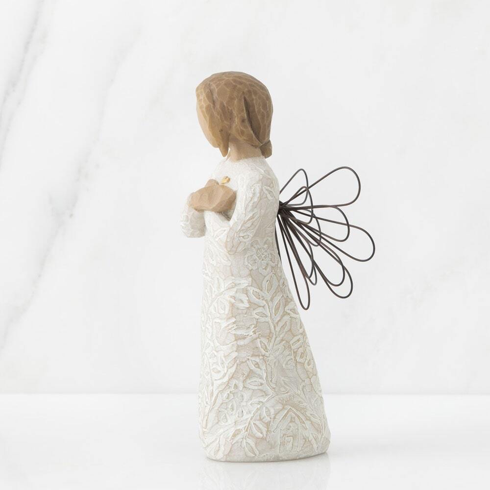 Standing angel in cream dress with wire wings, with crossed hands under small gold-leaf heart. Dress carved with symbols of nature