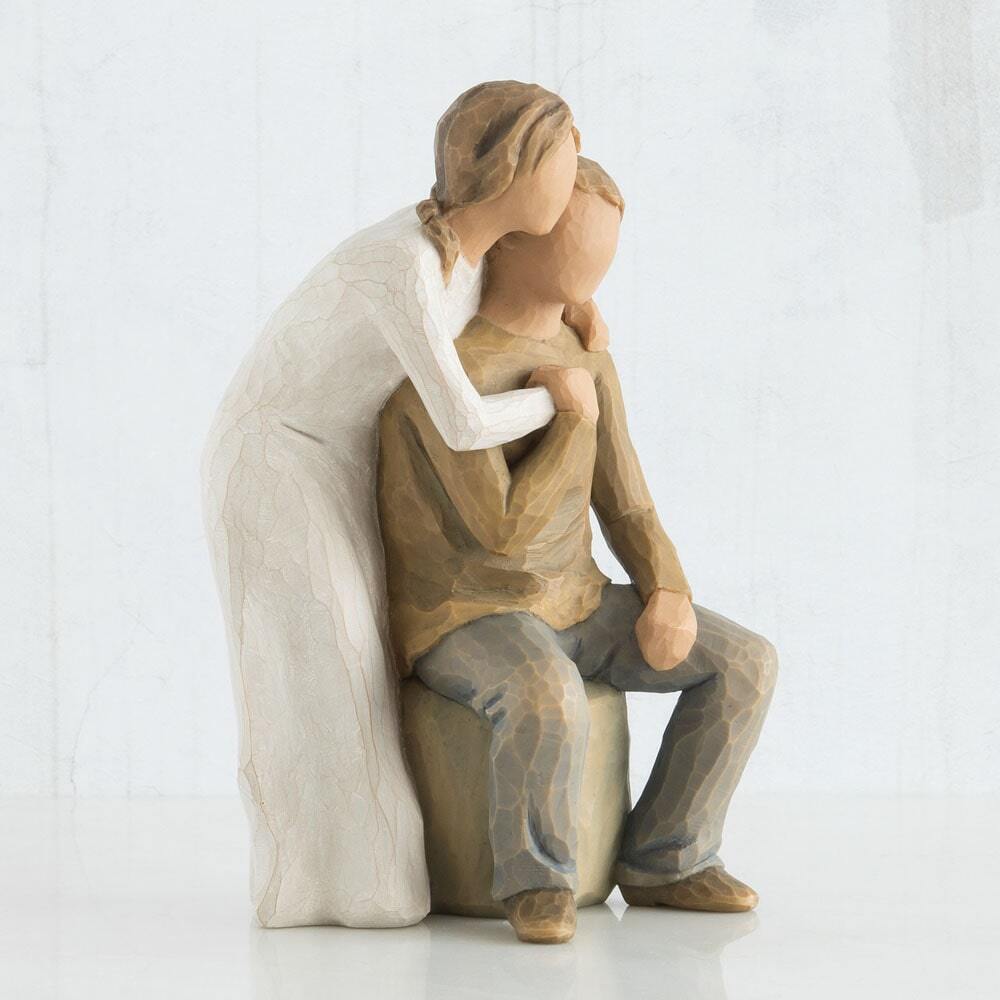 Figure of male and female couple; seated male in taupe shirt with blue jeans, female in cream dress, standing behind male, with arms around neck