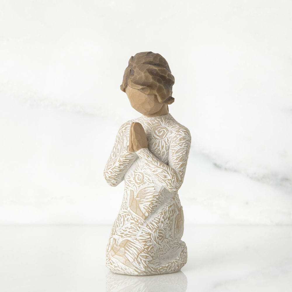 Kneeling female figure in cream dress with hands in prayer pose. Dress is heavily carved with birds and flowers