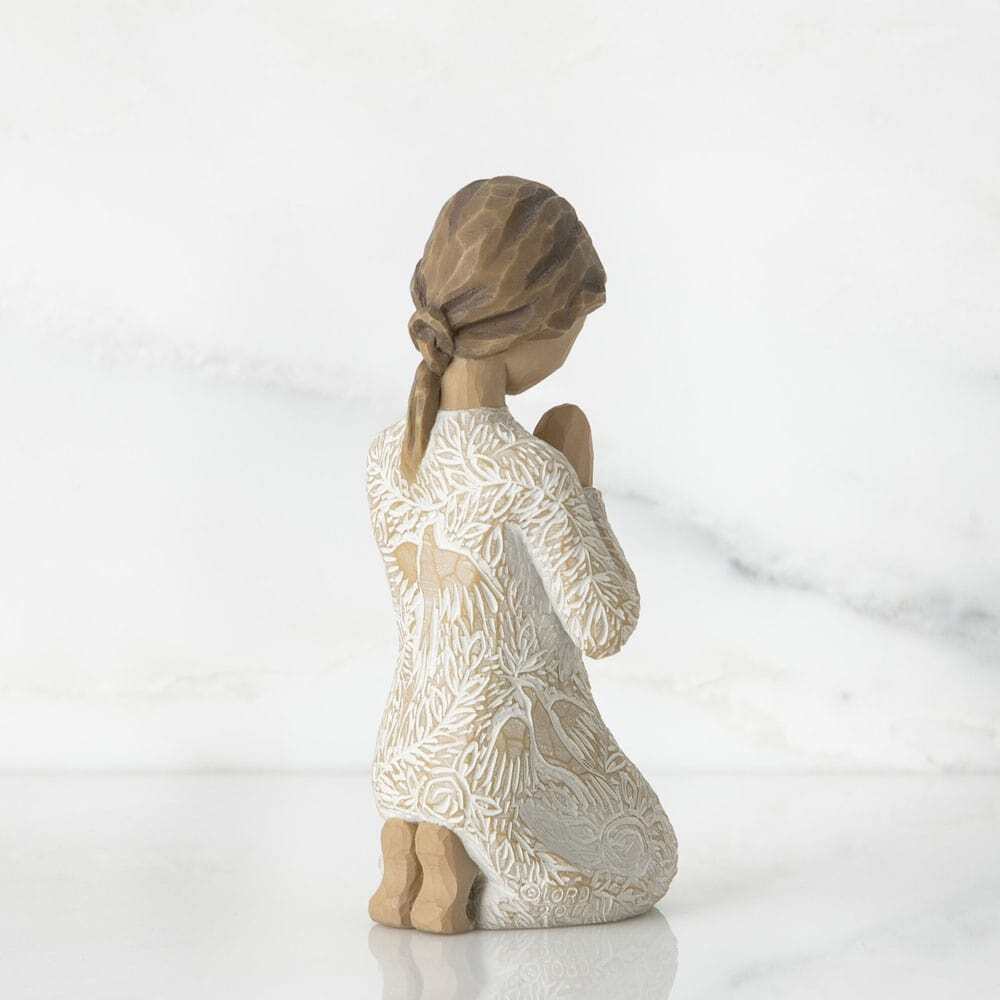 Kneeling female figure in cream dress with hands in prayer pose. Dress is heavily carved with birds and flowers