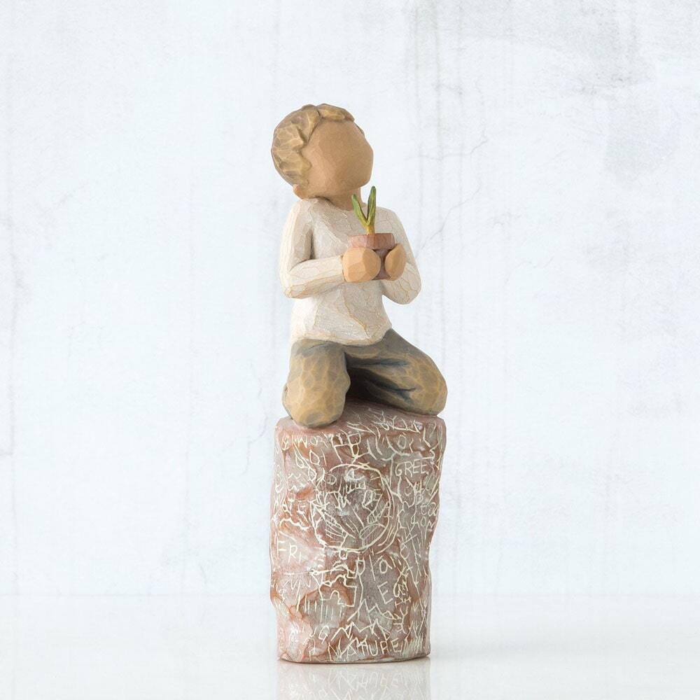 Figure of small boy in cream shirt and blue jeans holding a small green plant in terracotta pot, kneeling on tall red rock, etched with words and imagery of earth, nature and puzzle pieces