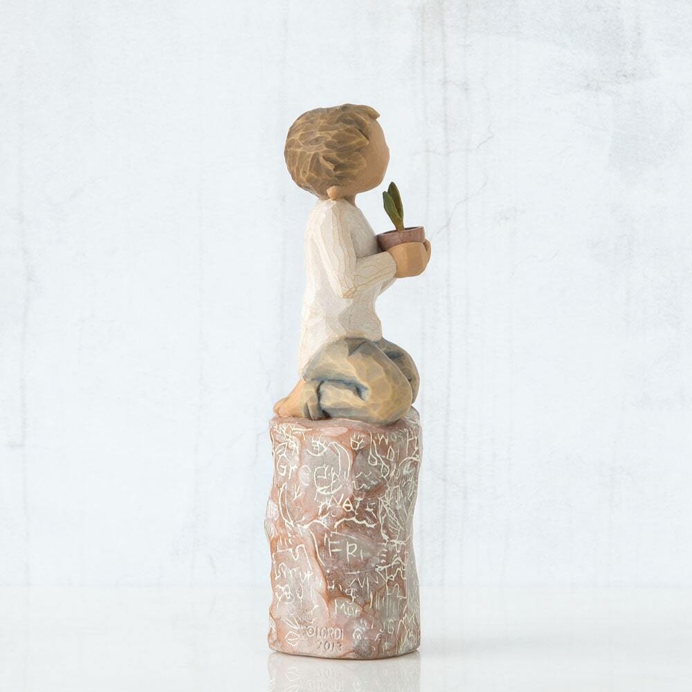 Figure of small boy in cream shirt and blue jeans holding a small green plant in terracotta pot, kneeling on tall red rock, etched with words and imagery of earth, nature and puzzle pieces