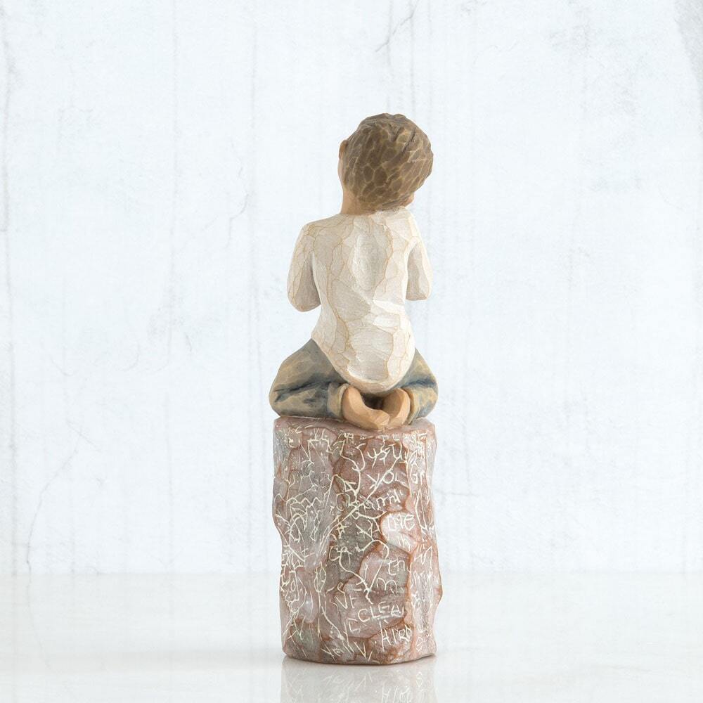 Back View: Figure of small boy in cream shirt and blue jeans holding a small green plant in terracotta pot, kneeling on tall red rock, etched with words and imagery of earth, nature and puzzle pieces